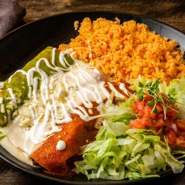 A plate of enchiladas, one green and one red, with rice, lettuce, and pico de gallo.