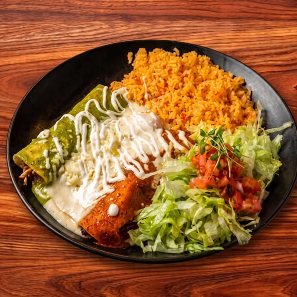 A black plate with two enchiladas, rice, and a side salad on a wooden table.